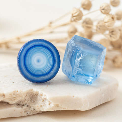 Gros plan d’une agate bleue polie accompagnée d’un morceau de calcédoine bleue brute, montrant leurs bandes concentriques et leurs textures naturelles sur une pierre claire.