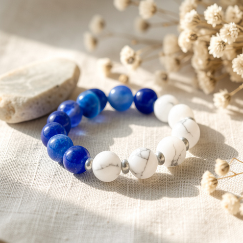 Bracelet composé de perles d’apatite bleue et de howlite blanche veinée, présenté sur un tissu en lin clair avec des éléments naturels.