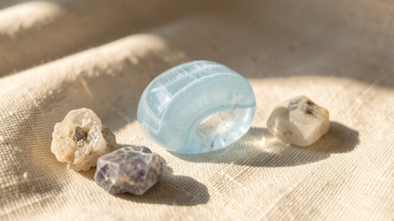 Gros plan d’une pierre de calcédoine bleu pâle polie, posée sur du lin naturel avec quelques fragments minéraux, éclairée par une douce lumière matinale.